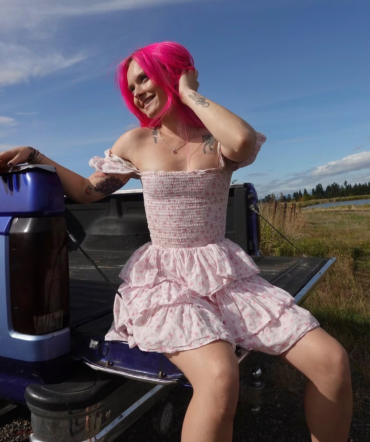 Savanna with bright pink hair, sitting on a truck tailgate in a floral dress